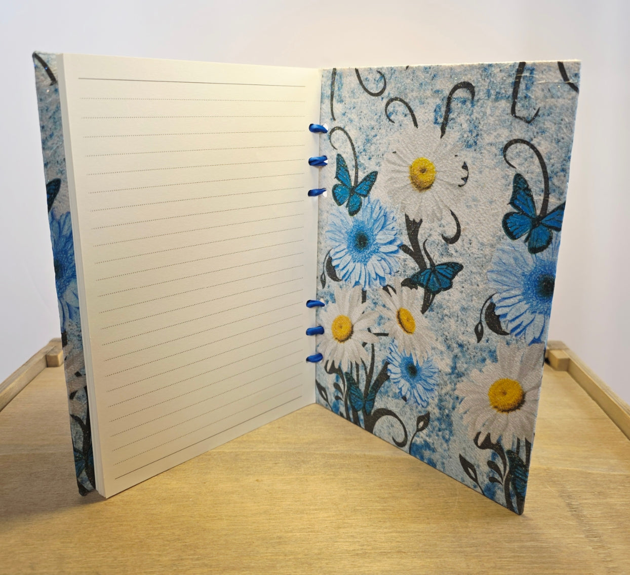 Notebook with floral and butterfly design on a wooden surface. white lined pages