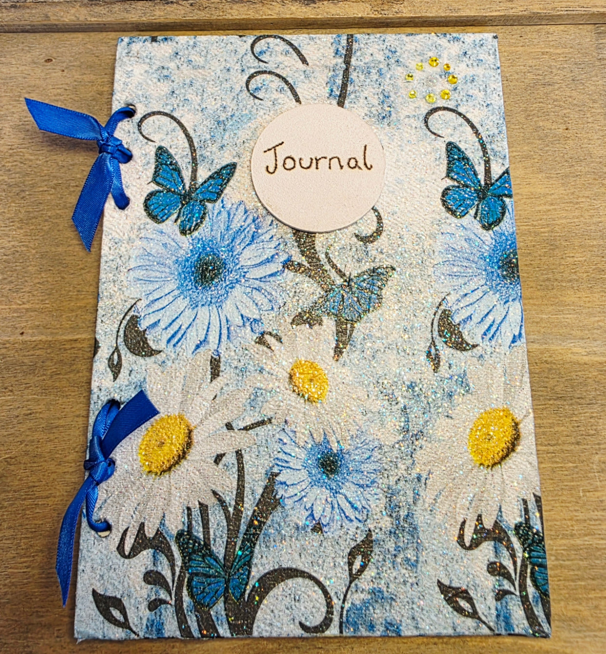 Decorative journal with floral and butterfly design on a wooden surface. blue ribbon bound