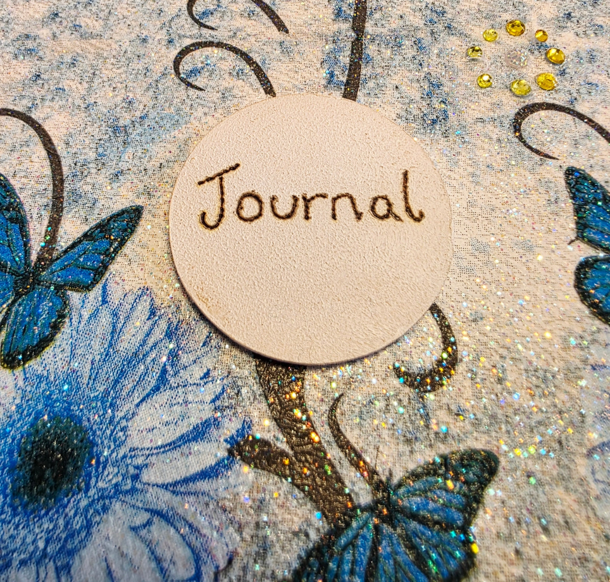 Decorative cover of a journal with blue butterflies and flowers, featuring a round label with 'Journal' text.