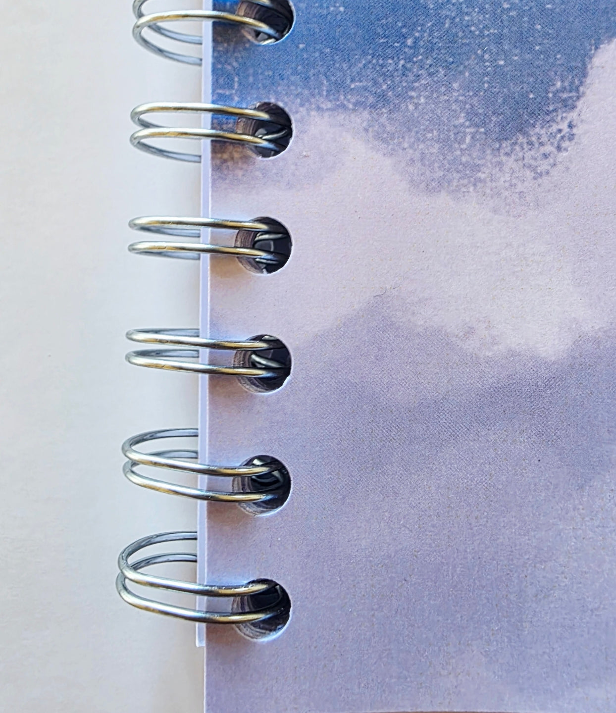 Close-up of a spiral-bound notebook with a watercolor cloud design on the cover.