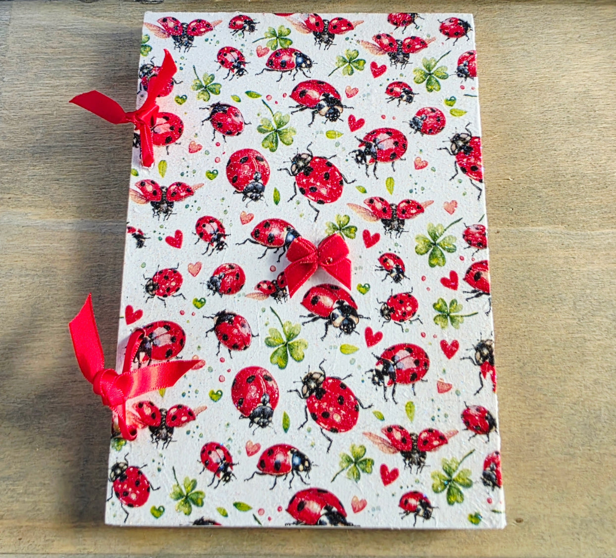 Notebook with ladybug pattern and bound with red ribbon on a wooden surface