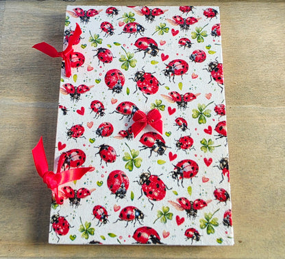 Notebook with ladybug pattern and bound with red ribbon on a wooden surface