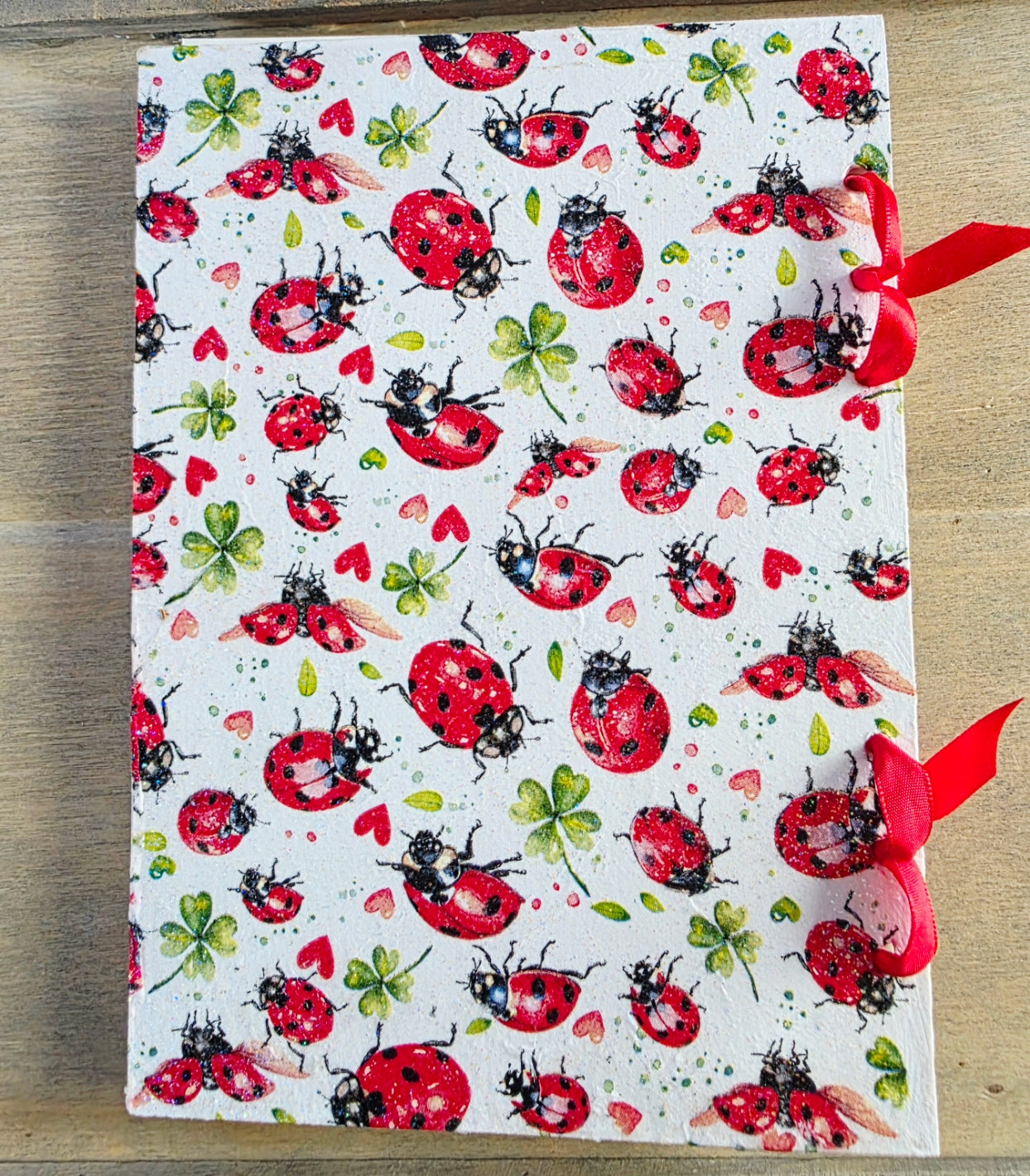Notebook with ladybug pattern and bound with red ribbon on a wooden surface