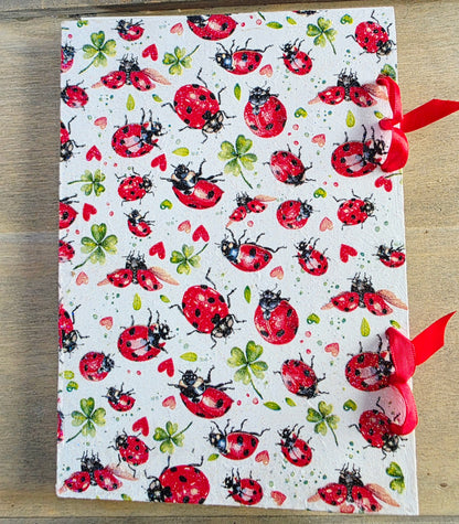 Notebook with ladybug pattern and bound with red ribbon on a wooden surface