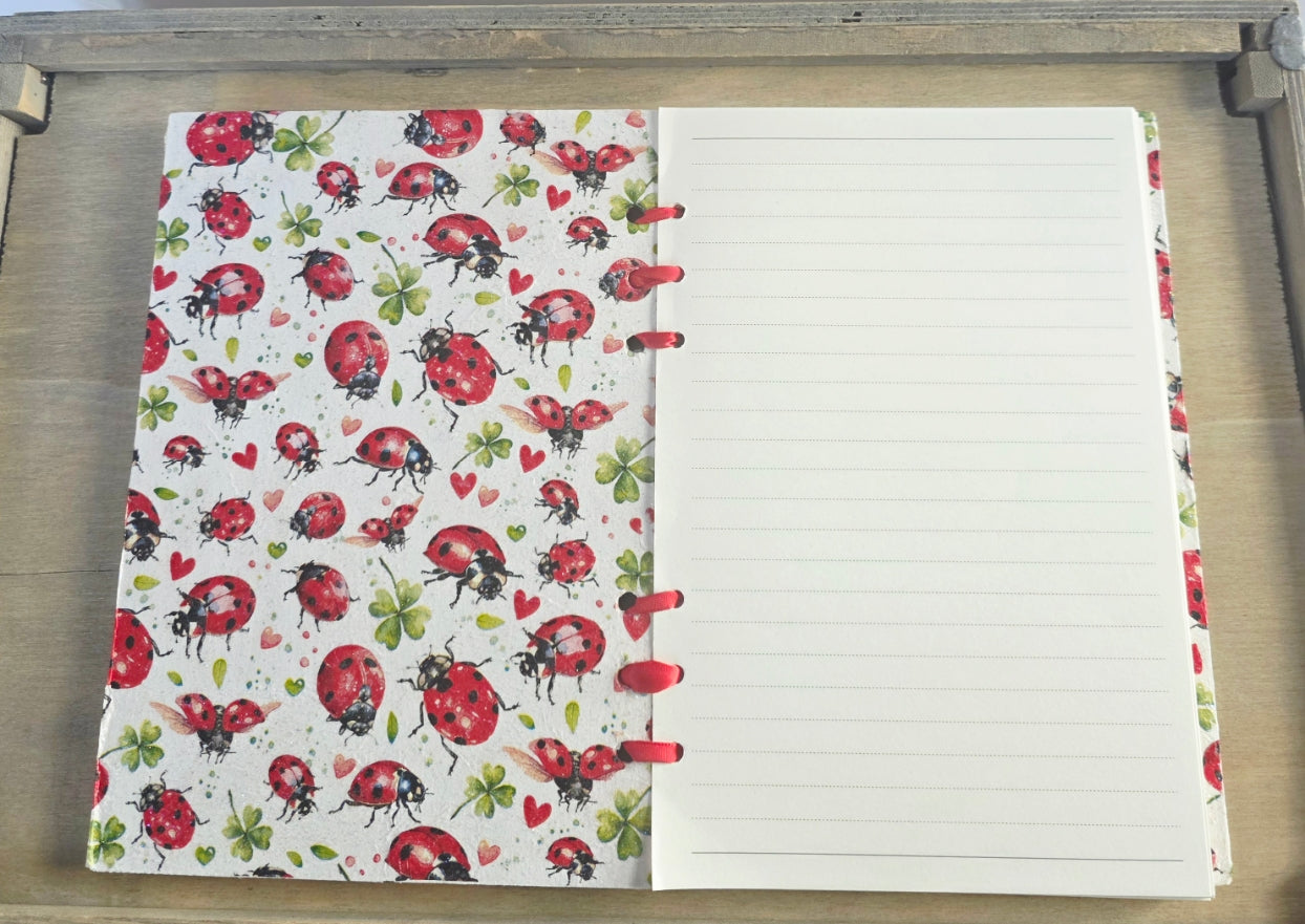 Notebook with ladybug pattern on the cover and lined pages. Bound with red ribbon