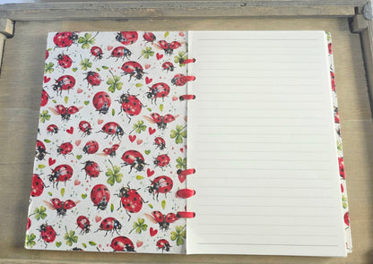 Notebook with ladybug pattern on the cover and lined pages. Bound with red ribbon