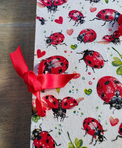 Notebook with ladybug and heart pattern and a bound with red ribbon on a wooden surface