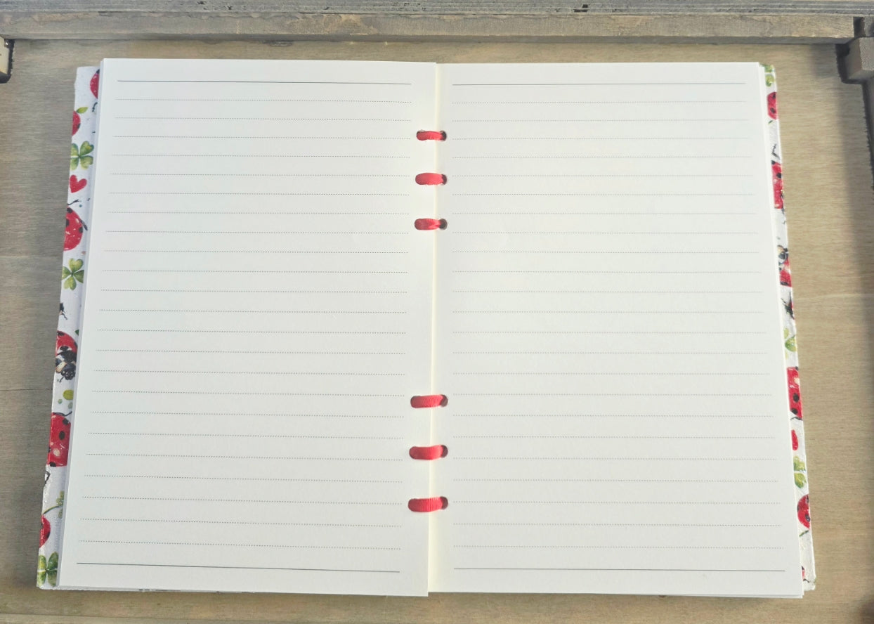 Open notebook with lined pages on a wooden surface. Bound with red ribbon