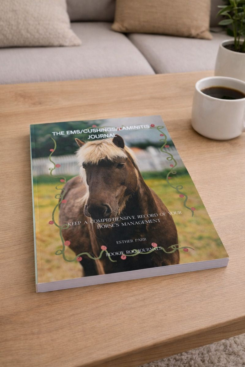 Paperback journal titled 'The Ems/Cushing's Laminitis Journal' on a wooden table with a cup of coffee.