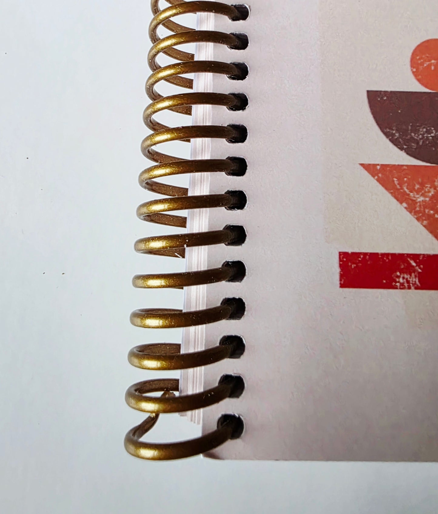 Close-up of a gold spiral binding on a notebook with a red abstract design in the background.