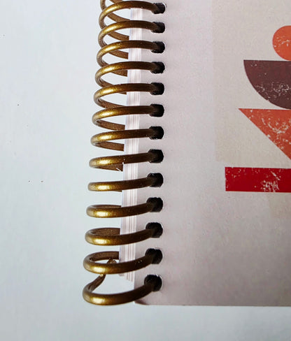 Close-up of a gold spiral binding on a notebook with a red abstract design in the background.