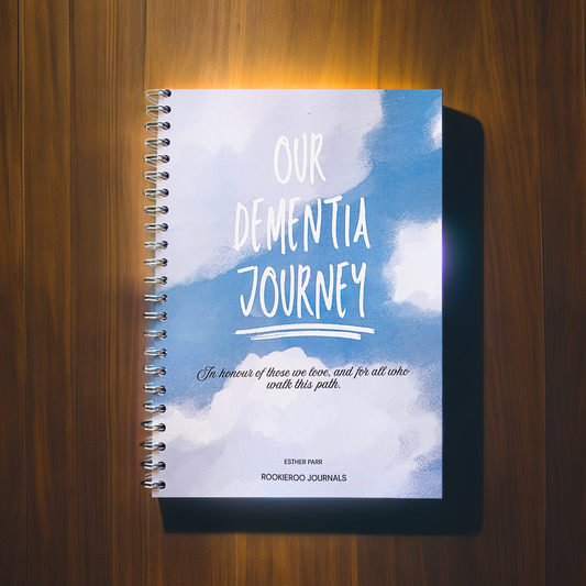 Journal with blue cover with white clouds titled Our dementia Journey. Silver wire binding and brand name Rookieroo Journals