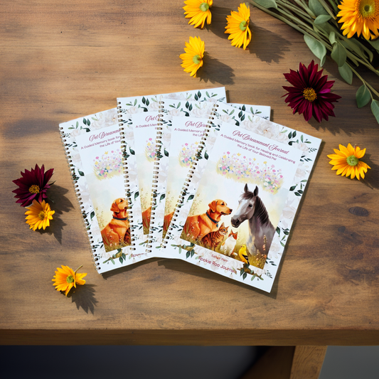 Four spiral-bound Pet bereavement journals on a wooden surface with flowers around them