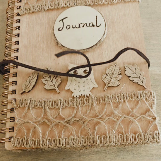 Video of a Wooden journal with decorative woodland elements and burlap design top and bottom. Dark brown faux suede tie. Round journal sign on the front. Spiral bound