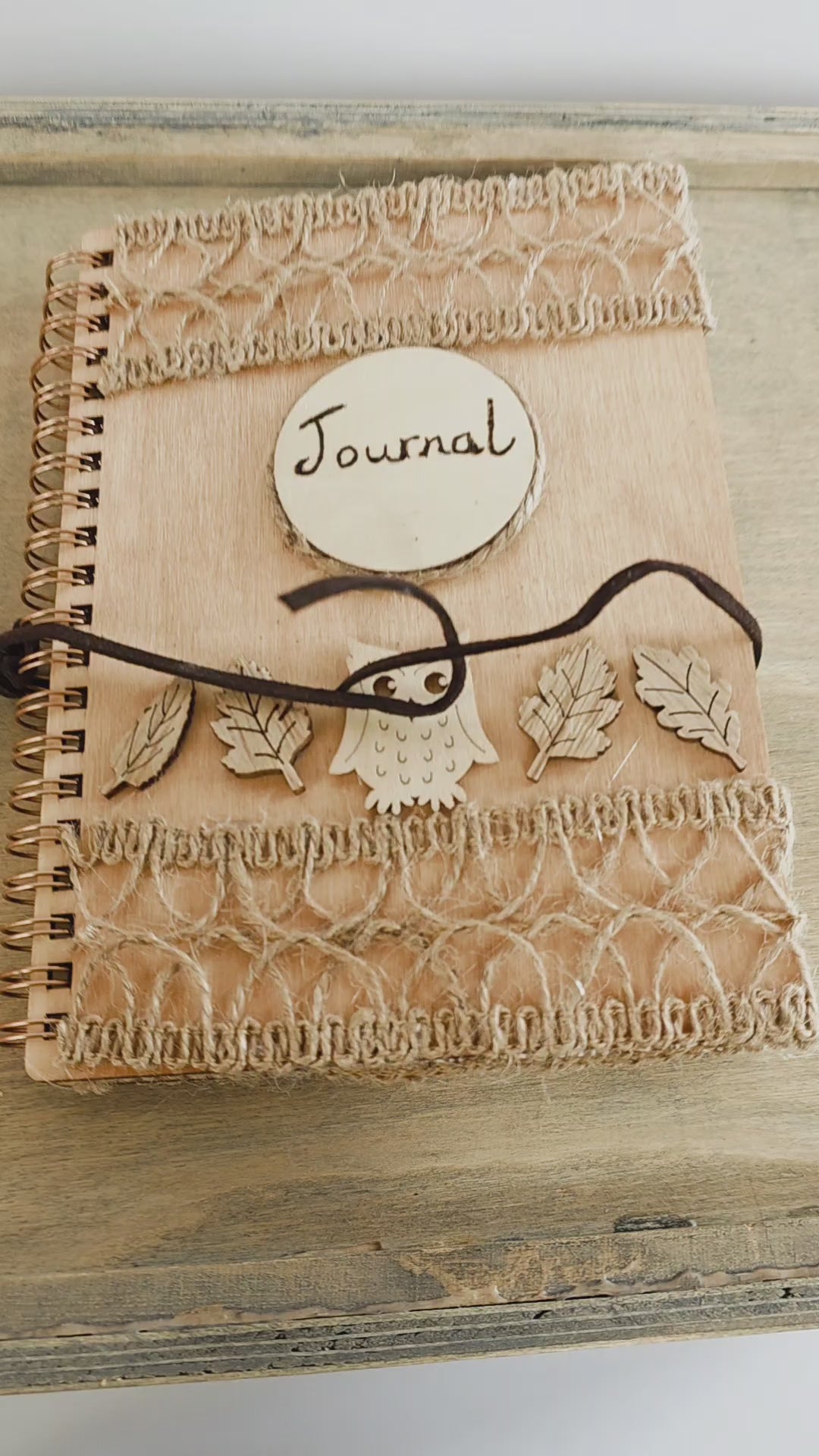 Video of a Wooden journal with decorative woodland elements and burlap design top and bottom. Dark brown faux suede tie. Round journal sign on the front. Spiral bound