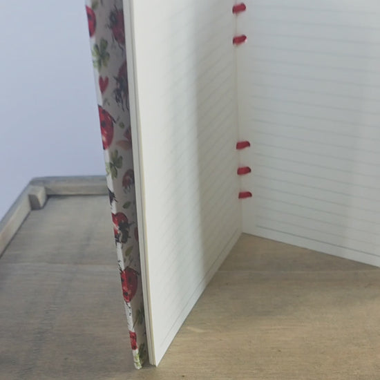 video of a ladybird themed notebook, showing inside lined pages and bound with red ribbon