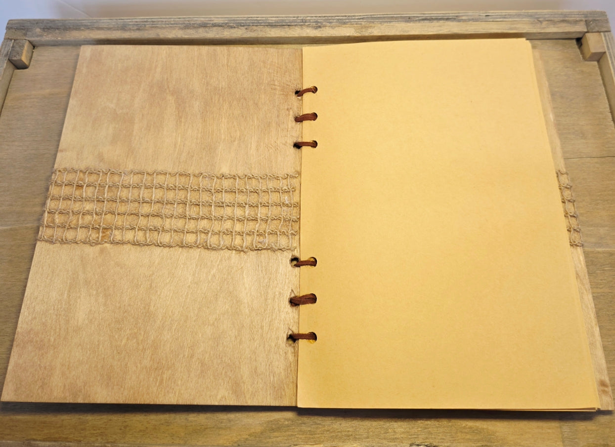 Open notebook with wooden cover on a wooden surface. Beige plain pages. Burlap across the inner cover