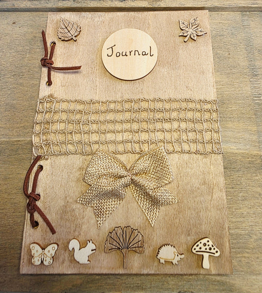 Journal with decorative woodland elements and a burlap mesh across the middle.  inside a wooden box on a textured surface.