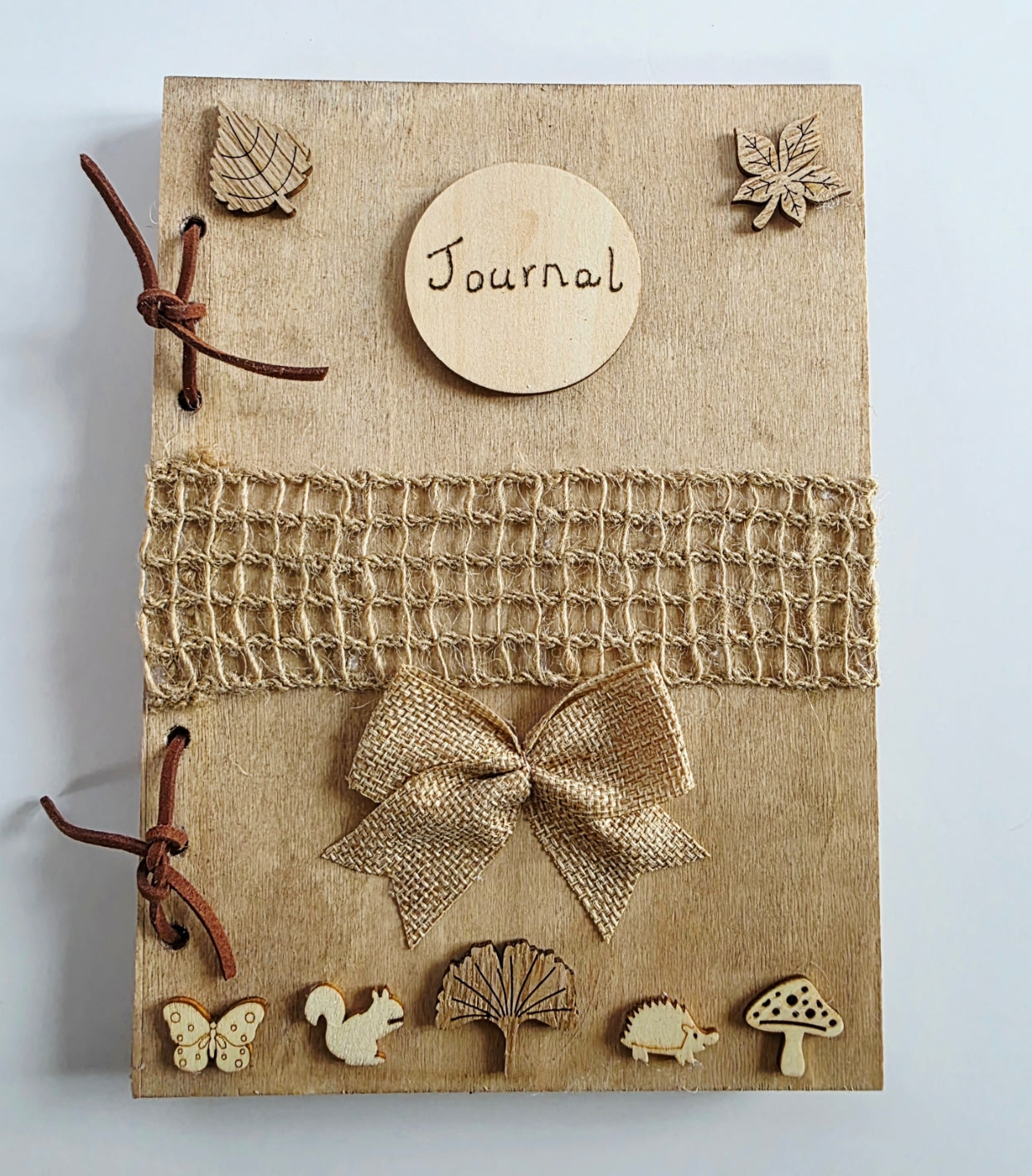 Journal with decorative woodland elements and a burlap mesh across the middle.  inside a wooden box on a textured surface.