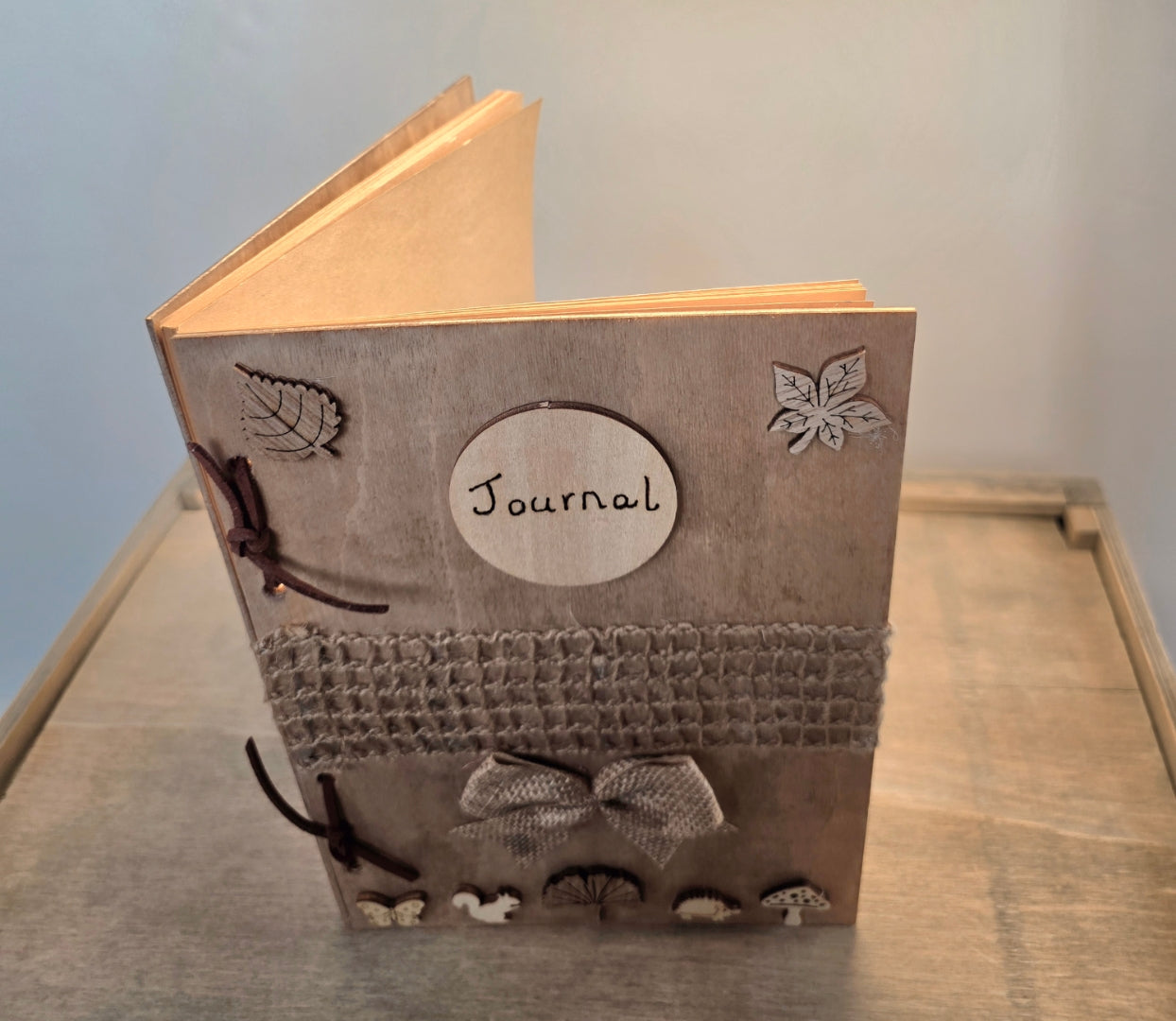 Journal with decorative woodland elements and a burlap mesh across the middle.  inside a wooden box on a textured surface.
