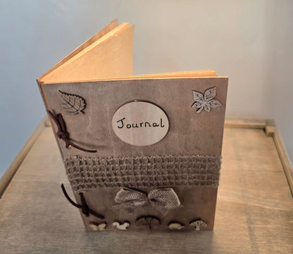 Journal with decorative woodland elements and a burlap mesh across the middle.  inside a wooden box on a textured surface.