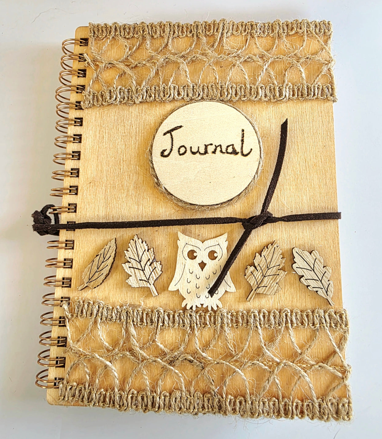 Wooden journal with decorative woodland elements and burlap design top and bottom. Dark brown suede tie. Round journal sign on the front. Spiral bound