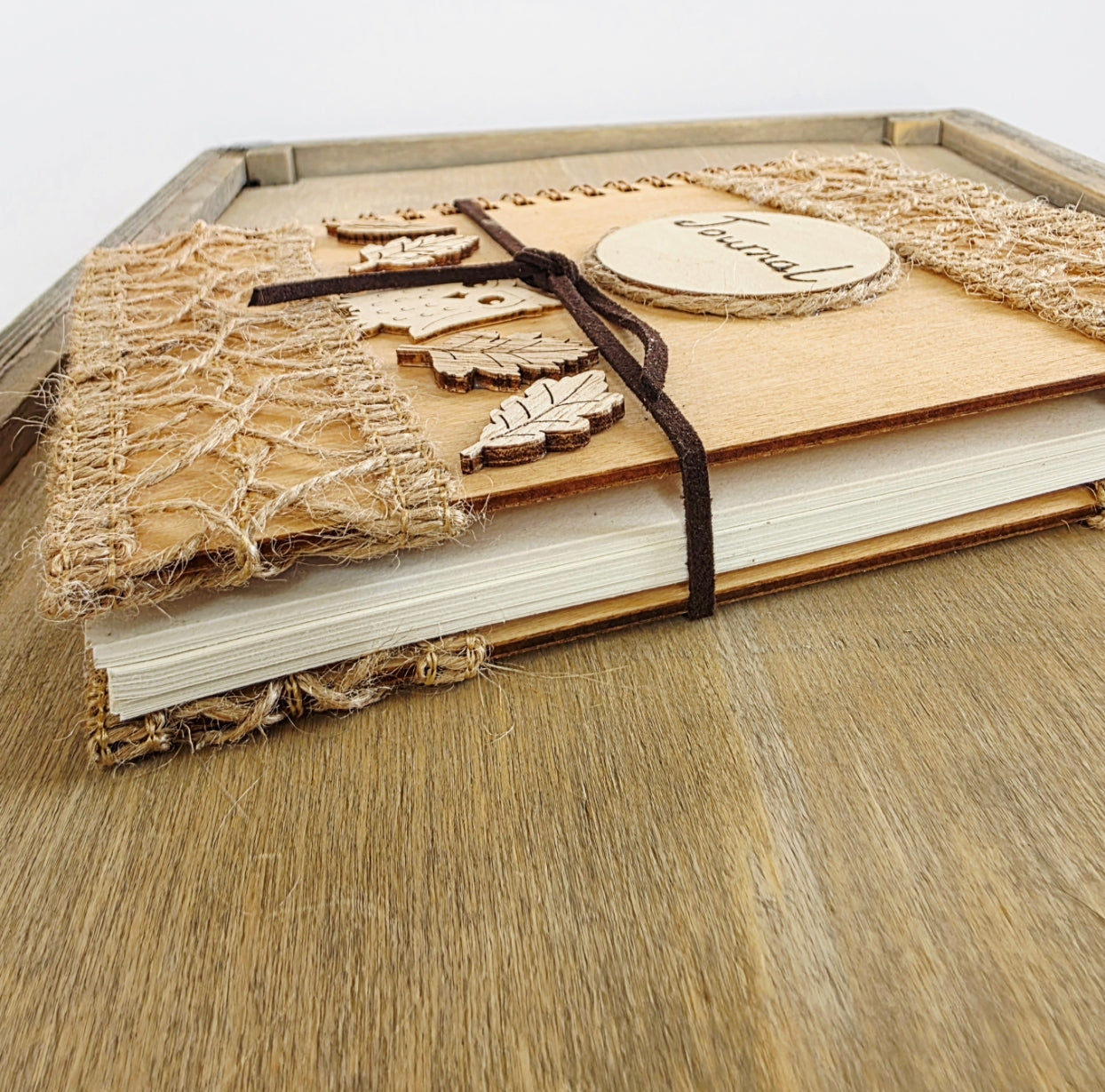 Wooden journal with decorative woodland elements and burlap design top and bottom. Dark brown faux suede tie. Round journal sign on the front. Spiral bound. Show lying flat with pages seen