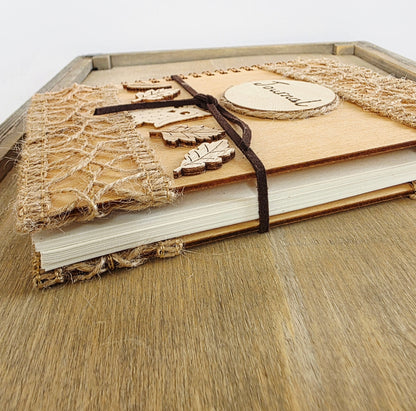 Wooden journal with decorative woodland elements and burlap design top and bottom. Dark brown faux suede tie. Round journal sign on the front. Spiral bound. Show lying flat with pages seen