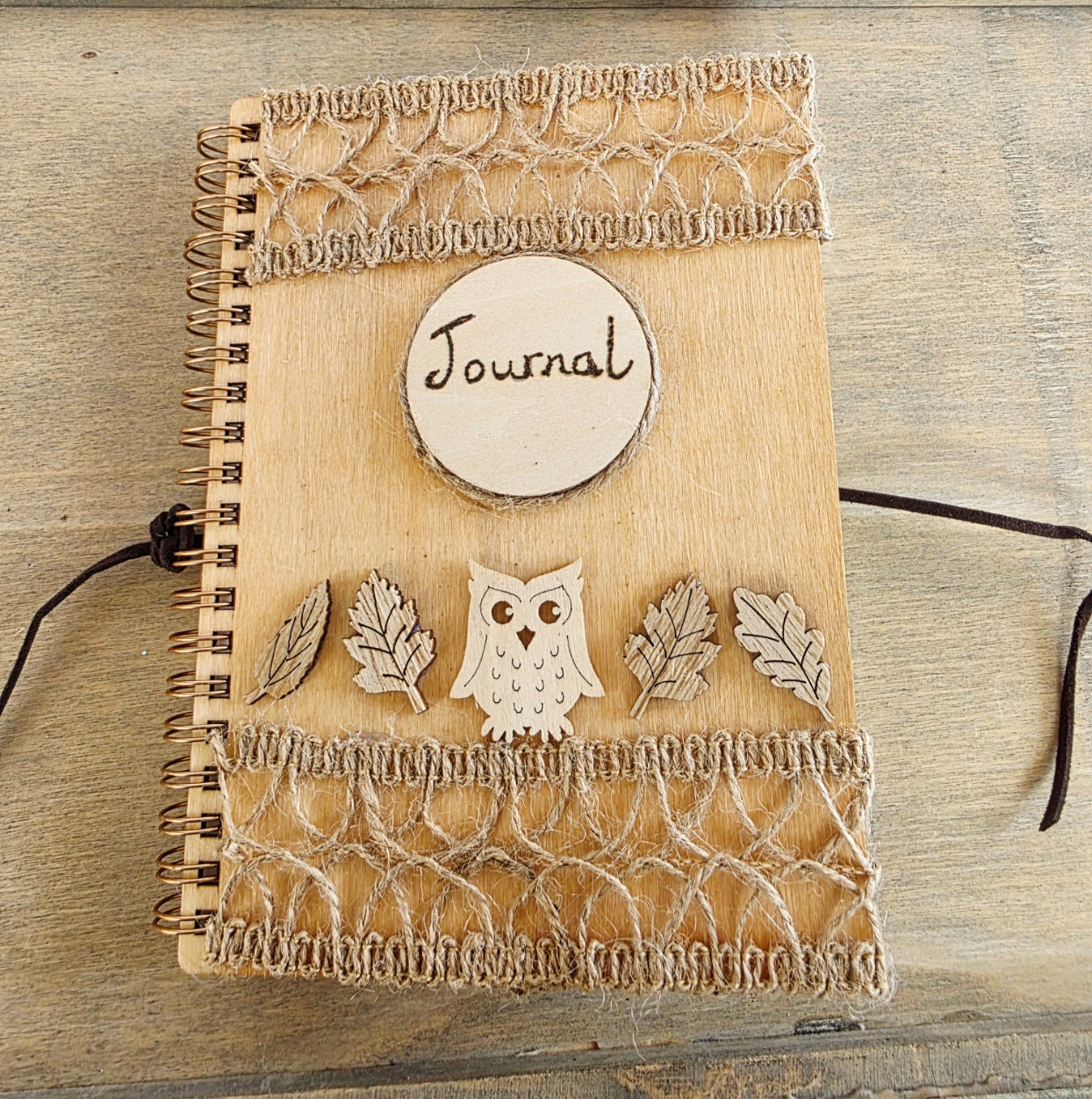 Wooden journal with decorative woodland elements and burlap design top and bottom. Dark brown faux suede tie. Round journal sign on the front. Spiral bound