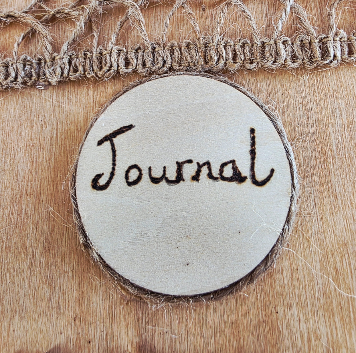 Round wooden sign with 'Journal' engraved on it, twine around the edge on the front of a wooden notebook